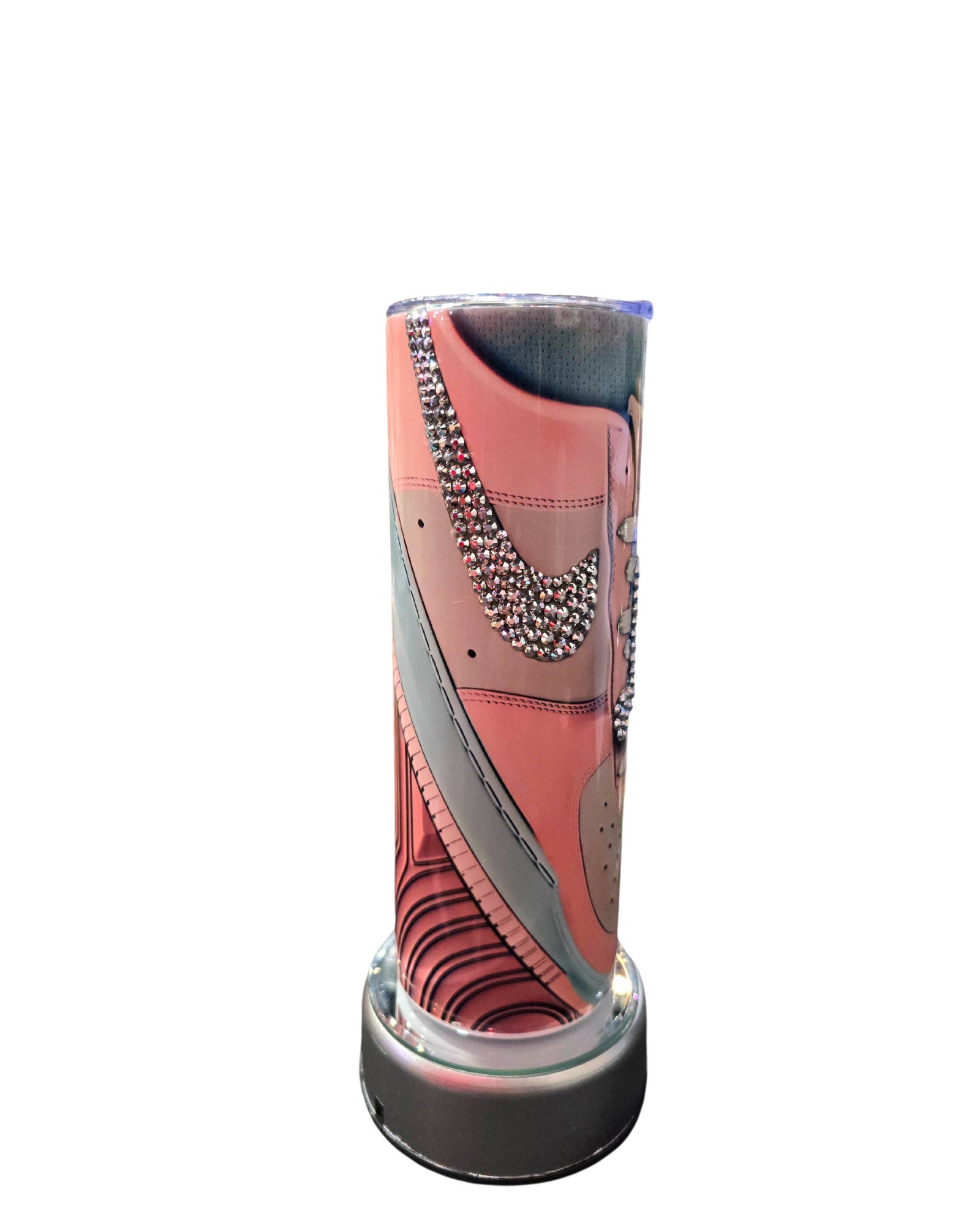 The 20oz Stainless Steel Rhinestone Tumbler Nike Inspired by Just For Lookz showcases a close-up design of a shoe, prominently featuring a studded Nike swoosh on a pink background. The bottom of the tumbler has a metallic finish. This stylish and contemporary tumbler is enhanced with rhinestone decorations for an added touch of elegance.